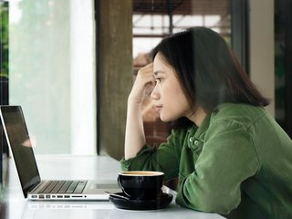 Eine Studentin schaut konzentriert auf einen Laptop; neben dem Laptop steht eine Tasse Kaffee.